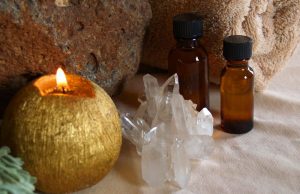 gold candle with quartz crystal and two bottles of essential oil